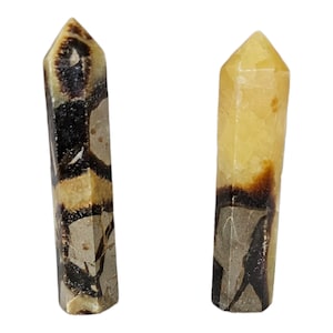 May include: Two polished stone towers with hexagonal points. The left tower features a tan and grey base with dark brown, web-like inclusions. The right tower has a translucent yellow top section transitioning into a tan, grey, and dark brown base.