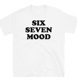 May include: White t-shirt featuring the words "SIX SEVEN MOOD" in large, bold, black lettering. The shirt has a crew neck and short sleeves. The text is centrally positioned on the front.