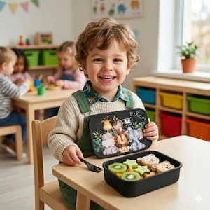 May include: A black rectangular lunchbox with a colorful jungle animal design, including a giraffe, lion, and elephant. The lunchbox is held by a child, and a matching container with food is on the table. The name "Ethan" is written on the lunchbox.