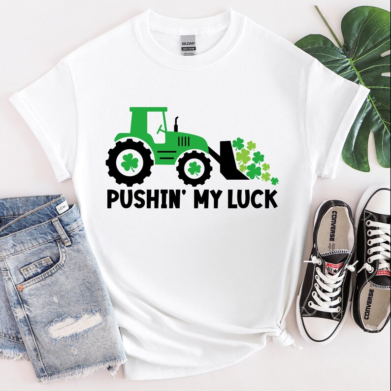 K&ouml;nnte beinhalten: Wei&szlig;es T-Shirt mit einem gr&uuml;nen Traktor und Kleebl&auml;ttern sowie dem Text "Pushin' My Luck".