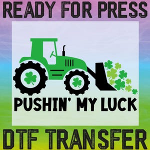 K&ouml;nnte beinhalten: Ein gr&uuml;ner Traktor mit einer schwarzen Schaufel, die einen Haufen gr&uuml;ner Kleebl&auml;tter schiebt. Der Text "Pushin' My Luck" befindet sich unter dem Traktor und "DTF Transfer" darunter.