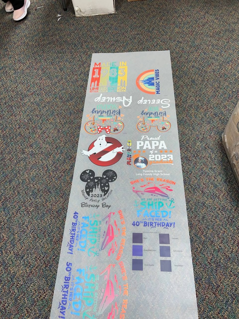 Peut inclure: Une feuille d'autocollants imprim&eacute;s avec divers motifs et textes. Les motifs incluent un logo Ghostbusters, des oreilles de Mickey Mouse et des phrases comme "Proud Papa of 2023" et "Ship Faced !" en plusieurs couleurs. La feuille comprend &eacute;galement des &eacute;chantillons de couleurs.
