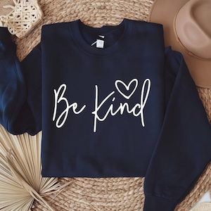 May include: A navy blue sweatshirt with the text "Be Kind" in white script with a small white heart above the word "Kind".