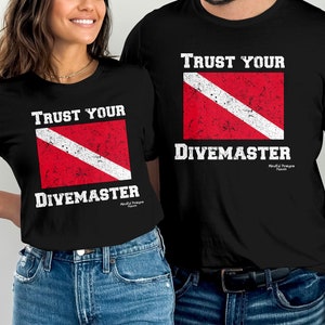 May include: Two black t-shirts with a red and white scuba diving flag and the text "Trust Your Divemaster".