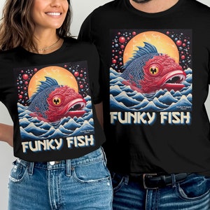 Puede incluir: Dos camisetas negras con una ilustración colorida de un pez funky con una boca roja y escamas azules y rojas. El texto "Funky Fish" está impreso en letras azules y blancas en las camisetas.
