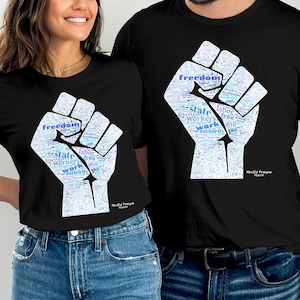 Op de afbeelding: Twee zwarte T-shirts met een afbeelding van een gebalde vuist gemaakt van woorden. De woorden omvatten "vrijheid", "staat", "arbeid", "arbeiders", "werk" en "autoriteit".