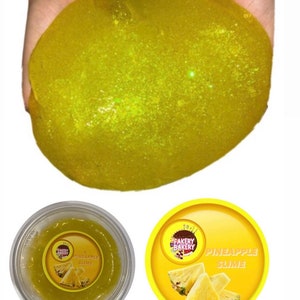May include: Yellow glitter slime in a clear container with a yellow label that says "Fakery Bakery Pineapple Slime".