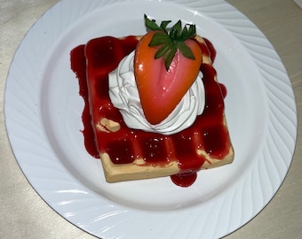 May include: A waffle topped with whipped cream and a strawberry, drizzled with red sauce on a white plate.