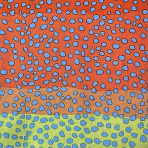May include: A textile fabric featuring a horizontal ombre gradient transitioning from pink to orange to yellow to green. The entire surface is covered in a repeating pattern of small, irregular light blue spots that vary in size and shape across the fabric.