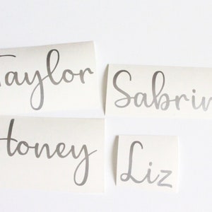 May include: Four white labels with silver lettering. The names Taylor, Sabrina, Honey, and Liz are written in cursive.