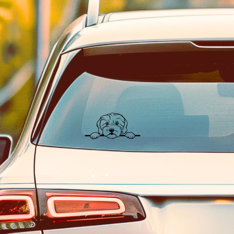 K&ouml;nnte beinhalten: Schwarzer Vinyl-Autoaufkleber mit einer stilisierten Illustration eines Hundes, der &uuml;ber eine horizontale Linie blickt. Der Hund hat ein flauschiges Aussehen mit detaillierten Gesichtsz&uuml;gen. Der Aufkleber ist auf der Heckscheibe eines wei&szlig;en Autos angebracht.
