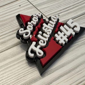 Op de afbeelding: Een zwart, rood en wit driehoekig bord met de woorden "Soror Felishia #445" in witte letters.