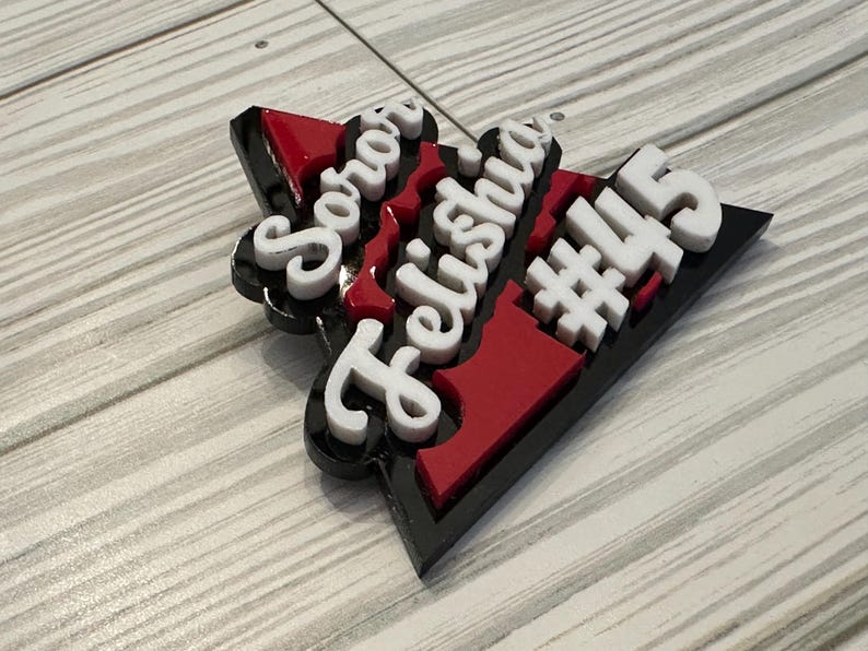 Op de afbeelding: Een zwart, rood en wit driehoekig bord met de woorden "Soror Felishia #445" in witte letters.