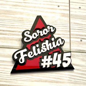 Op de afbeelding: Een zwart driehoekig bord met een rode binnenkant. Het bord heeft witte tekst met de tekst "Soror Felishia #45".