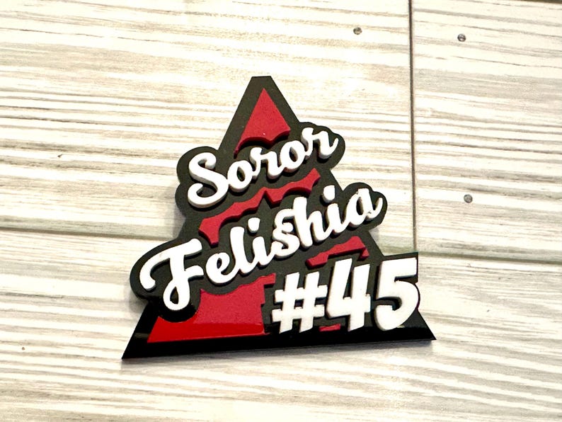 Op de afbeelding: Een zwart driehoekig bord met een rode binnenkant. Het bord heeft witte tekst met de tekst "Soror Felishia #45".