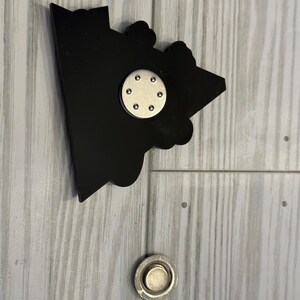 Op de afbeelding: Zwarte en zilveren magnetische pin met een cartoon afbeelding van een huis. De pin heeft een ronde magneet aan de achterkant.