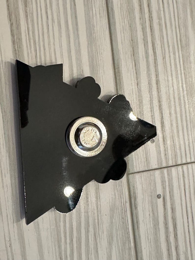 Op de afbeelding: Zwart-witte cartoon-personage magneet met een zilveren magnetische achterkant. De magneet is gevormd als een huis met een puntdak.