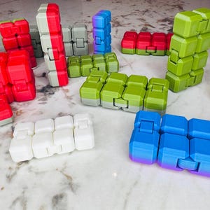 Può includere: Una collezione di giocattoli sensoriali colorati in plastica. I giocattoli sono di varie forme e dimensioni, tra cui cubi, quadrati e rettangoli. I colori includono rosso, verde, blu, bianco e grigio.
