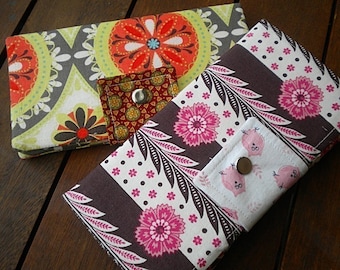May include: Two fabric wallets with different patterns. One wallet has a brown, white, and pink floral pattern. The other wallet has a gray, green, and orange floral pattern.