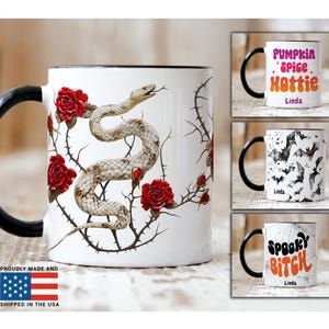 May include: White ceramic mugs with black handles. One mug features a snake and red roses design. Other mugs have the phrases "Pumpkin Spice Hottie" and "Spooky Bitch", and a bat pattern. All mugs are proudly made and shipped in the USA.