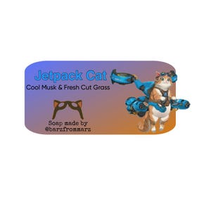 以下が含まれることがあります： ジェットパックを装着した漫画の猫が描かれた石鹸。石鹸のラベルには「Jetpack Cat」と「Cool Musk & Fresh Cut Grass」と書かれています。ラベルには「Soap made by @barzfrommarz」の文字も含まれています。猫はオレンジと白で、青いジェットパックをしています。