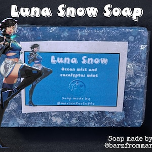 May include: A blue and white soap bar featuring a cartoon character on the front. The soap is labelled "Luna Snow" and states "Ocean mist and eucalyptus mint". The soap is made by @maracutestuffs and @barzfrommarz.
