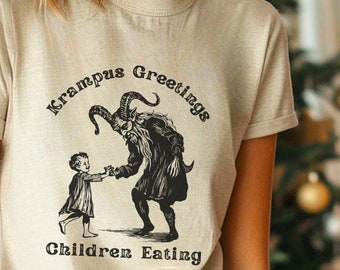 Puede incluir: Camiseta beige con el texto "Krampus Greetings" y una ilustración negra de Krampus y un niño. La camiseta está hecha de un material suave y es adecuada para ropa casual. La palabra "NATURAL" está en un círculo en la esquina superior izquierda.