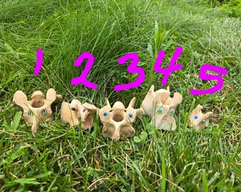 May include: Five white animal bones with googly eyes, arranged in a row on a bed of green grass. The bones are numbered 1 through 5 in pink.