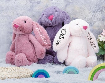 May include: Three plush bunny rabbits in pink, purple, and white. Each bunny has long floppy ears, a pink nose, and embroidered details. One bunny has the name "Olivia" embroidered on its ear, and the other two have the date "2025.02.11" on their ears.