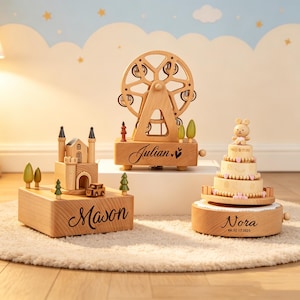 May include: Three wooden music boxes with light wood grain. One features a castle and the name Mason, one a ferris wheel and the name Julian, and one a tiered cake with a bear topper and the name Nora with the date 02.17.2025 printed on the base.