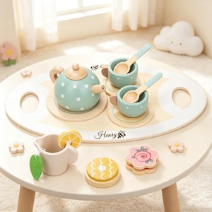 May include: A wooden tea set featuring a sage green teapot with white polka dots, two matching cups with light blue spoons, a white creamer with a lemon slice, and a serving tray personalized with the name Henry and a party hat graphic.