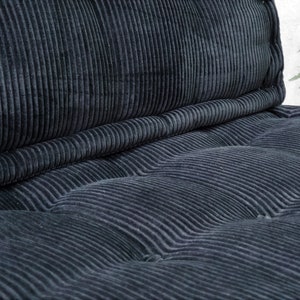 Puede incluir: Un coj&iacute;n de terciopelo de pana negro con un dise&ntilde;o capiton&eacute;. El coj&iacute;n est&aacute; hecho de una tela suave y mullida y tiene una sensaci&oacute;n c&oacute;moda.