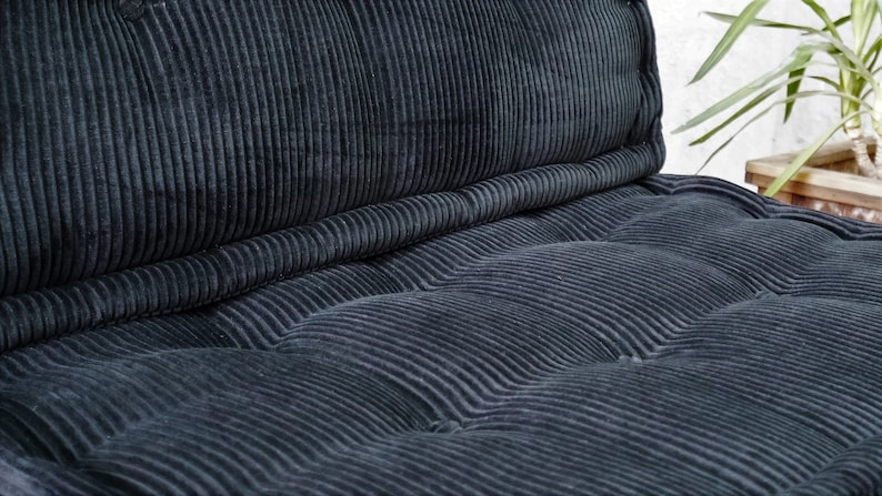 Puede incluir: Un coj&iacute;n de terciopelo de pana negro con un dise&ntilde;o capiton&eacute;. El coj&iacute;n est&aacute; hecho de una tela suave y mullida y tiene una sensaci&oacute;n c&oacute;moda.