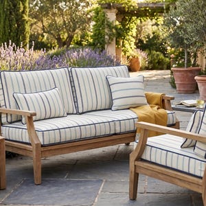 Può includere: Set di sedute da esterno in legno con cuscini a righe blu e bianche. Il set comprende un divano a due posti, una poltrona e cuscini. Una coperta gialla è drappeggiata sul divano.