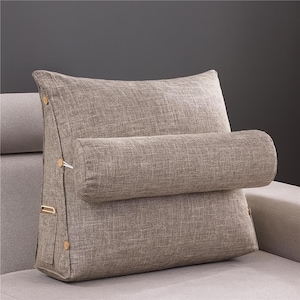 May include: A beige backrest pillow with a cylindrical bolster. The pillow has a textured fabric and wooden button details. It is designed to provide support and comfort while sitting or reclining. The pillow is on a light grey sofa.