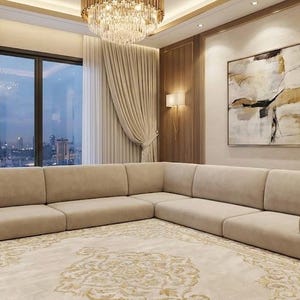 Puede incluir: Un salón moderno con un gran sofá esquinero beige sobre una alfombra estampada. La habitación tiene grandes ventanales con vistas a la ciudad, cortinas beige y una lámpara de araña. Una pintura abstracta cuelga de la pared.