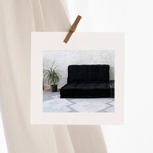 Puede incluir: Un sof&aacute; fut&oacute;n negro con una alfombra gris debajo. El fut&oacute;n est&aacute; en una habitaci&oacute;n con una pared blanca y una planta en una maceta.
