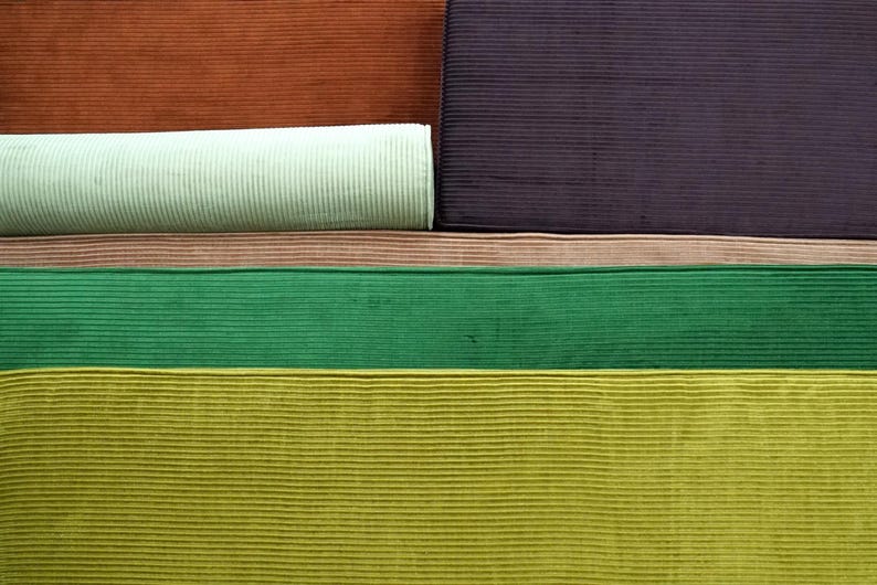 May include: A collection of corduroy fabric swatches featuring a variety of colors including rust orange, deep purple, light mint green, soft pink, vibrant emerald green, and chartreuse yellow, all displaying a distinct vertical ribbed texture.
