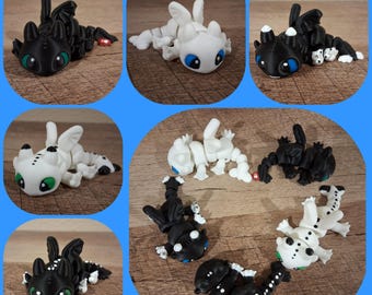 Puede incluir: Una colección de pequeñas figuras de dragones detalladas en varias poses. Los dragones son principalmente negros y blancos, con ojos verdes y azules. Algunos tienen manchas. Las figuras están dispuestas sobre una superficie de madera.