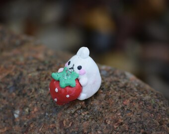 May include: A white ceramic figurine of a bunny holding a red and green strawberry. The bunny has pink cheeks and black eyes.