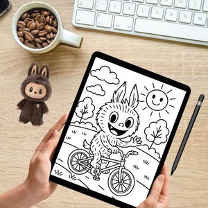 Puede incluir: Ilustraci&oacute;n digital en blanco y negro de un conejo de dibujos animados montando en bicicleta en una tableta. La imagen incluye un sol sonriente y &aacute;rboles. Tambi&eacute;n se ve un l&aacute;piz &oacute;ptico y un juguete de peluche.
