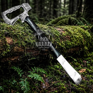 Könnte beinhalten: Eine weiße Keramiktasse mit schwarzem Henkel und dem Text "But first, coffee" in schwarzer, handschriftlicher Schrift. Die Tasse steht auf einer weißen Oberfläche.