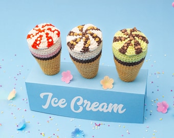 May include: Three crocheted ice cream cones in a blue box with the words "Ice Cream" printed on the front. The cones are decorated with different colored sprinkles and chocolate chips.