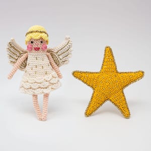 May include: A crocheted angel figurine with a white dress, gold wings, and a yellow halo. The angel is standing next to a yellow crocheted star.
