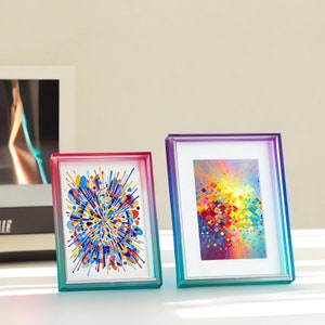 May include: Two colorful acrylic picture frames with a gradient of pink, purple, blue, and green. The frames are holding abstract paintings with a burst of color.