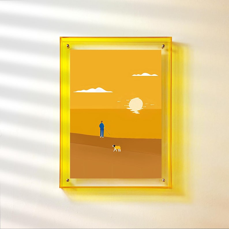 Peut inclure: Une impression d'art encadr&eacute;e repr&eacute;sentant un paysage minimaliste. L'&oelig;uvre d'art repr&eacute;sente une personne avec un chien sur une surface marron, avec un soleil couchant et des nuages en arri&egrave;re-plan. Le cadre est de couleur jaune vif.
