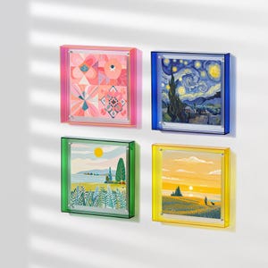 Puede incluir: Cuatro impresiones enmarcadas cuadradas con diferentes imágenes. Los marcos son de diferentes colores: rosa, azul, verde y amarillo. Las imágenes son un patrón geométrico, una escena de noche estrellada, un paisaje con un lago y árboles, y una puesta de sol sobre un campo.