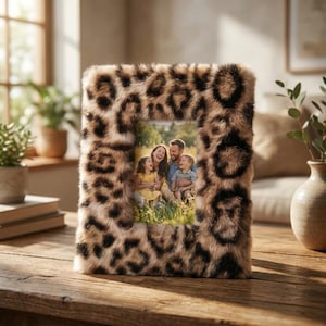 May include: A square photo frame with a faux fur leopard print design. The frame holds a family photo. The frame is on a wooden table, with a vase and plants in the background.
