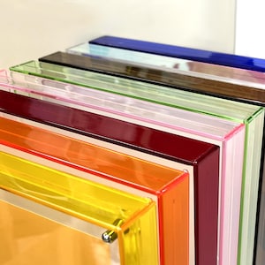 Peut inclure: Une pile de cadres en acrylique color&eacute;s, allant du jaune &agrave; l'orange, en passant par le rouge, le rose, le vert, le marron et le bleu. Les cadres, &agrave; la finition brillante, sont empil&eacute;s, r&eacute;v&eacute;lant leurs couleurs vives.