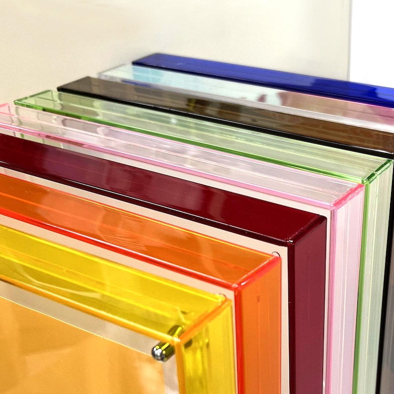 Peut inclure: Une pile de cadres en acrylique color&eacute;s, allant du jaune &agrave; l'orange, en passant par le rouge, le rose, le vert, le marron et le bleu. Les cadres, &agrave; la finition brillante, sont empil&eacute;s, r&eacute;v&eacute;lant leurs couleurs vives.